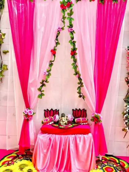 For this setup, the client wanted a pink theme. I used bright pink and white drapes, accented with green floral vines. The idol's asana is decorated with lotus flowers, creating a lovely and unique color combination for the festival.