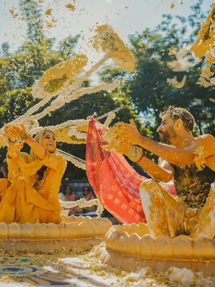 The bride and groom playfully throw haldi and flowers at each other during a joint ceremony.