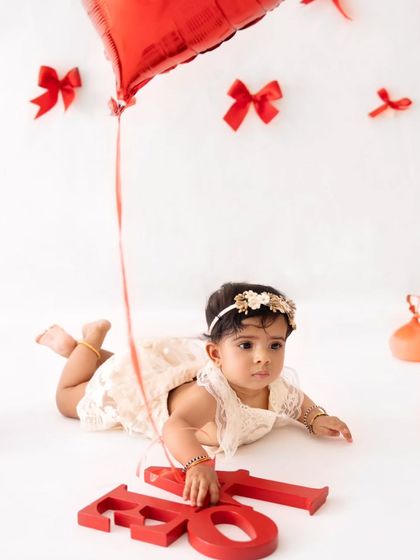 A baby girl explores the studio during her Valentine's Day shoot, featuring red bows and a heart-shaped balloon.