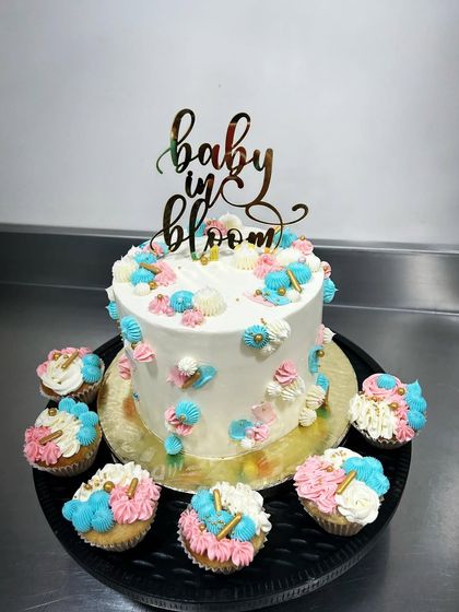 A "Baby in Bloom" celebration set featuring a main cake and matching cupcakes. The delicate floral piping in pink, blue, and white creates a beautiful garden theme for the special day.