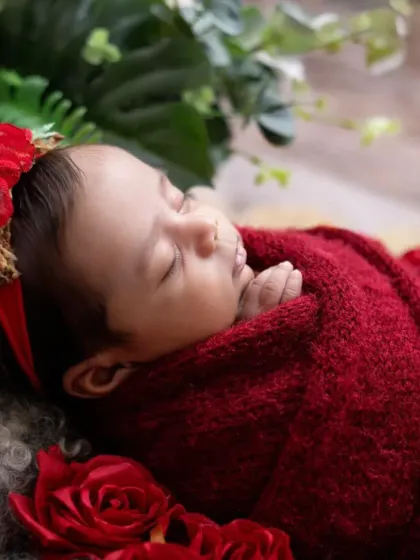 A side profile captures the sweet curve of a newborn's cheek and their tiny, pursed lips. The rich red tones make this image feel so warm and full of love.