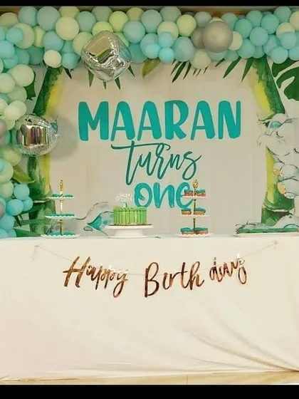 A stylish and modern first birthday party with a jungle theme. This setup includes a custom backdrop with the child's name, a beautiful organic balloon garland in mint green and silver, and a neatly arranged cake table, showing our ability to create chic and contemporary designs.