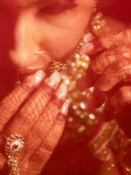 An artistic, warm-toned close-up of a bride, focusing on her henna-covered hands and nath.
