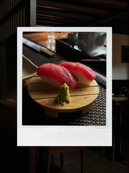 A simple yet perfect serving of Tuna Nigiri. This polaroid-style shot captures two pieces of rich Akami tuna on a traditional wooden sushi geta, highlighting the quality and authenticity of our ingredients.