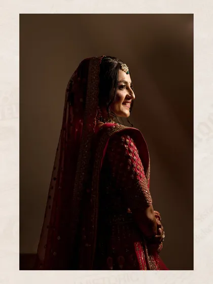 A beautiful bridal portrait using soft, dramatic lighting to highlight the bride's happy expression and her stunning red lehenga.