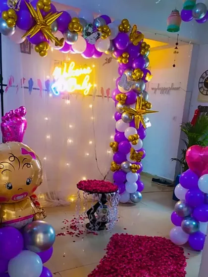 A "Welcome Baby" decoration in purple, gold, and silver, with a neon sign and a path of rose petals.