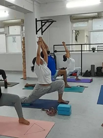 The energy in the room is focused as students move into Virabhadrasana I (Warrior I), guided by our experienced teacher.