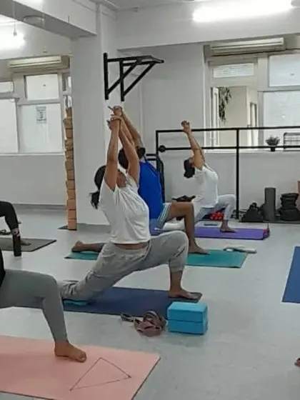 The energy in the room is focused as students move into Virabhadrasana I (Warrior I), guided by our experienced teacher.