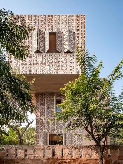 The House of Solid Stone in Jaipur, seen through the trees, showcases its operable stone screens. These jaalis are a modern interpretation of a traditional element, designed to modulate the harsh Rajasthani sun while creating intricate patterns of light within.