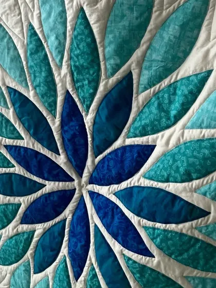A closer look at the artistry of the Sea Glass Quilt. The detailed leaf-shaped stitching, done on our professional longarm machine, adds a beautiful texture that complements the curved appliqué design.