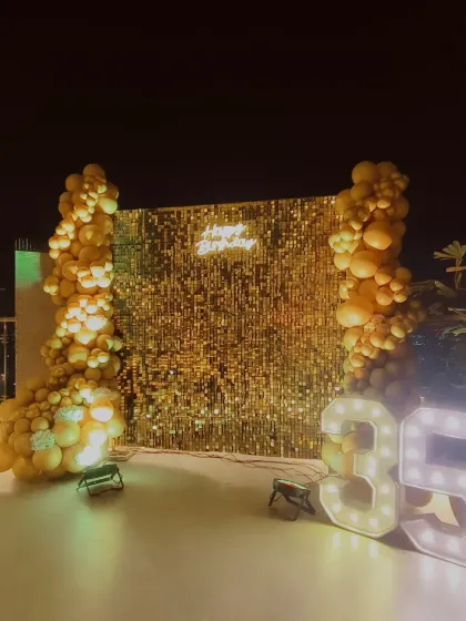 A glamorous all-gold theme for a 35th birthday. This outdoor setup features a full gold sequin wall, gold balloon columns, and large marquee numbers for a dazzling effect.
