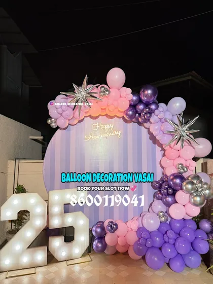 A unique anniversary backdrop with a striped purple and pink panel. The setup is framed by a balloon arch in matching colors and includes a large, illuminated "25" to celebrate a silver anniversary.