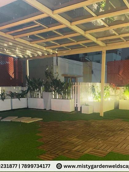 This wide shot of the Banashankari terrace shows the glass pergola structure and the arrangement of planters and seating. The design creates a space that feels both open and intimate.