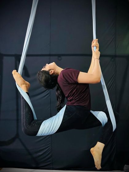 A student holds a graceful split pose supported by the aerial hammock, allowing for a deeper stretch while building balance.