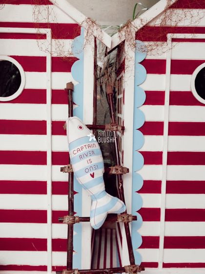 A custom-made fish-shaped pillow with the words 'Captain River is One!' hangs on a rustic ladder against the striped sailor cabin.