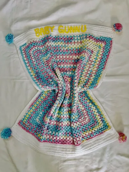 Another view of the personalized "Baby Gunnu" blanket, showing the playful pom-poms and the classic granny square design that will never go out of style.