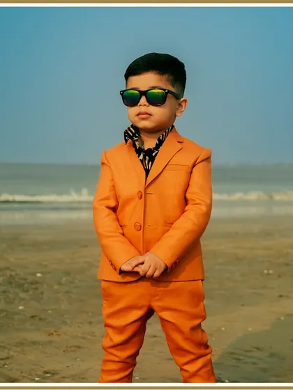 Bringing main character energy to his birthday shoot. This vibrant orange suit, paired with a patterned shirt, is a bold and stylish choice that perfectly captures his fun personality against a beautiful beach backdrop.