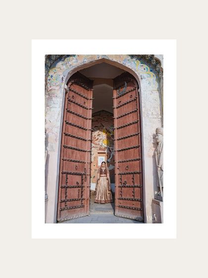 A wide shot of a bride standing in the grand entrance of Fort Neemrana, framed in white.