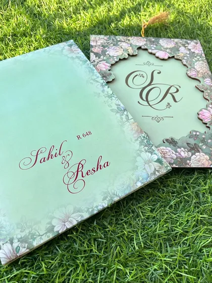 A close-up of the light green floral invitation, showcasing the elegant script and the beautiful contrast with the darker green laser-cut cover.
