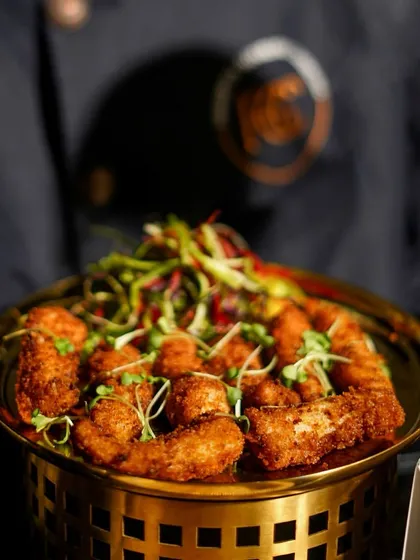 A golden bowl filled with crispy fried appetizers, garnished with fresh microgreens. This is an example of how we serve larger quantities of finger foods for guests to enjoy.