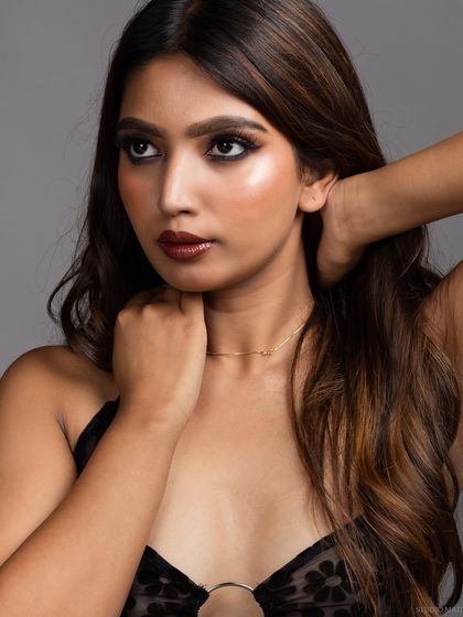 A close-up portrait of a model in a sheer black dress, with a thoughtful, sideways glance.