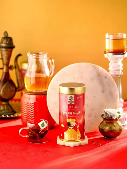 A vibrant and regal composition for Hindraj's Tangerine Thakur Tea. The bold red and gold background complements the packaging and creates a feeling of luxury and warmth.