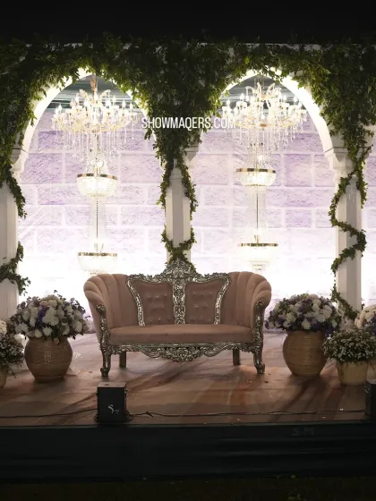A beautiful stage setup with a vintage-style sofa, set against a backdrop of white arches, columns, and crystal chandeliers.