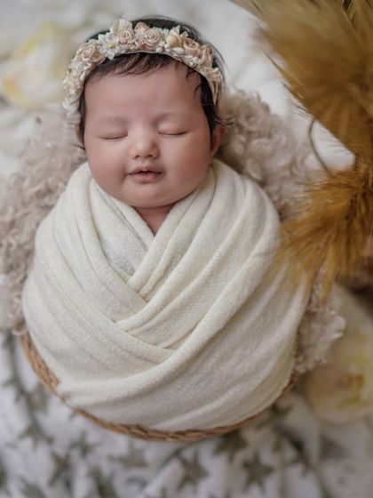 A boho dream. This baby is swaddled in a neutral wrap, surrounded by pampas grass and soft textures for a modern, earthy feel.