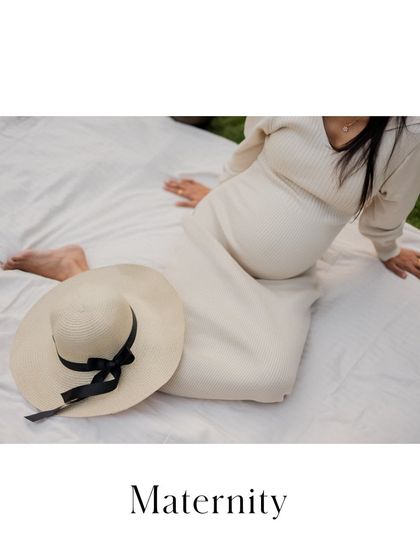 A serene moment captured during an outdoor picnic-style setup. The wide-brimmed hat adds a touch of elegance to this relaxed and peaceful maternity portrait.