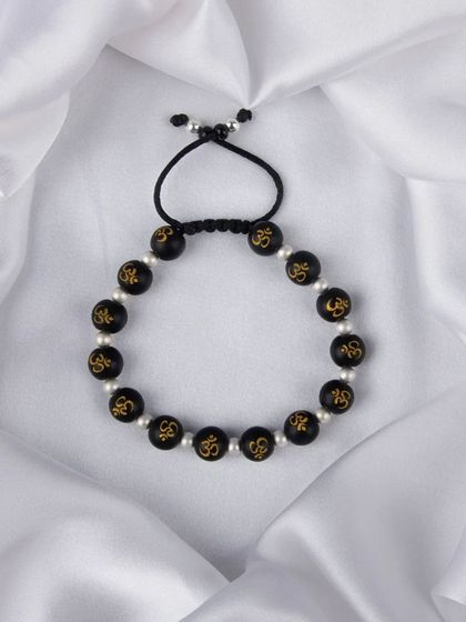 A spiritual bracelet with black beads featuring the 'Om' symbol, laid on a white satin cloth.