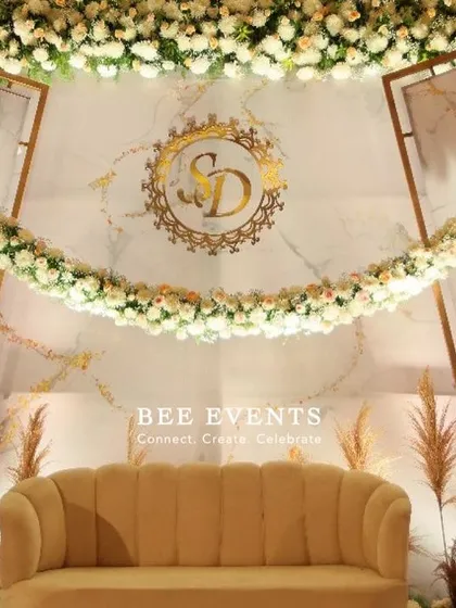A close-up of the elegant reception stage, focusing on the custom monogram and the beautiful arch of white flowers. The soft lighting and pampas grass accents add a touch of modern romance.