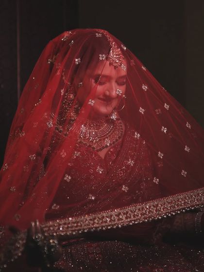 A classic bridal portrait showing the bride under her red veil. The soft lighting and her gentle smile create a timeless and serene image, full of grace and beauty.