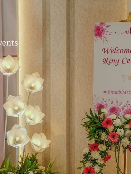 A personalized welcome sign for a Ring Ceremony, elegantly displayed on an easel and decorated with a beautiful arrangement of pink and white flowers.