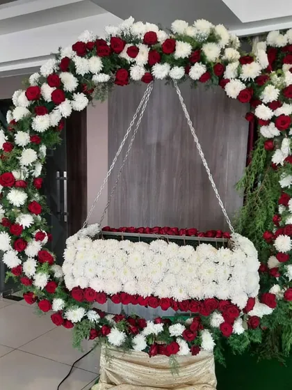 A circular floral arch with a hanging cradle, decorated with red roses and white chrysanthemums for a naming ceremony.