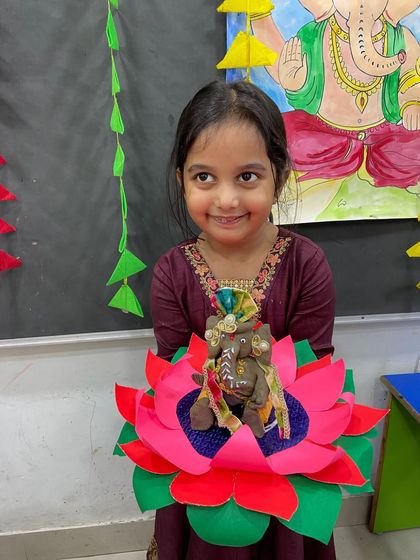 A smiling student holds her decorated Ganesha idol sitting on a vibrant, handmade paper lotus.