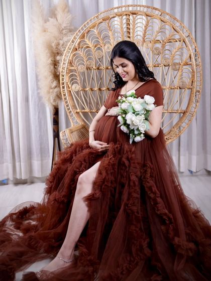 A serene moment in the peacock chair. The mom-to-be looks down at a bouquet of white flowers, creating a peaceful and beautiful composition.