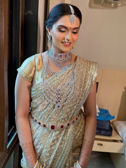 A smiling portrait of bride Trisha, showcasing her complete South Indian bridal look. The intricate jewellery, including the choker, layered necklace, and waist belt, are all perfectly coordinated.