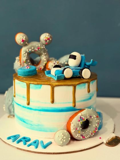 A fun doughnut-themed cake for Arav. This cake features a gold drip, a fondant race car, and of course, plenty of sprinkle-covered doughnuts.