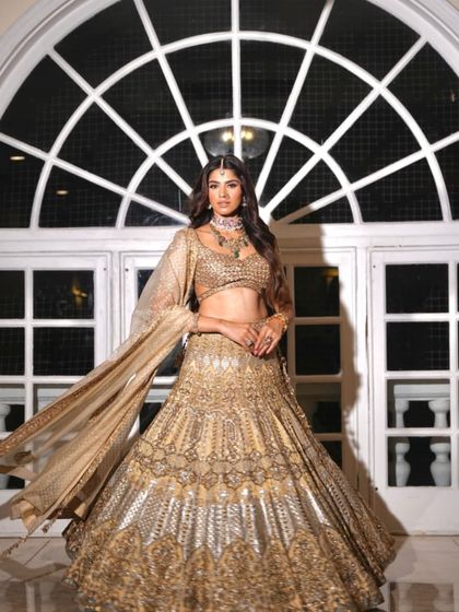 The flowing dupatta adds a touch of drama to this shimmering golden lehenga. A perfect shot against a grand architectural backdrop.