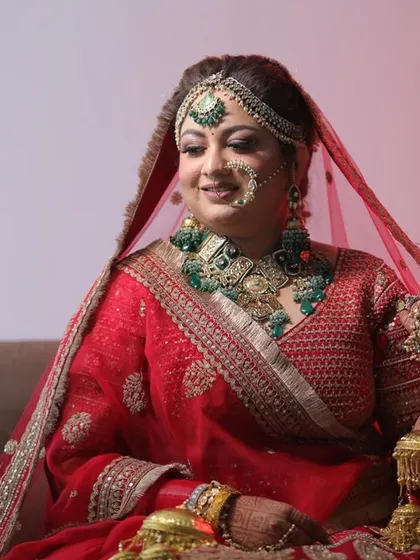 A beautiful bride in a classic red lehenga, wearing a heavy emerald and polki set that exudes royalty.