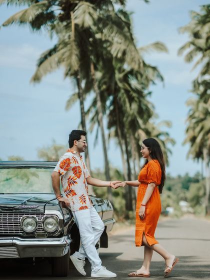 The couple shares a gentle moment, holding hands by their classic car on a tropical road. This image feels like a still from a romantic movie.