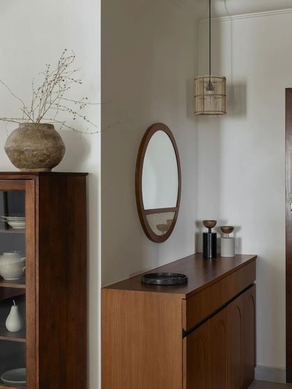 This foyer design is an example of Japandi principles: minimal, natural, and warm. A simple shoe unit and an oval mirror are complemented by wooden rafters on the ceiling. Nothing here overwhelms; instead, you are embraced by a sense of calm.