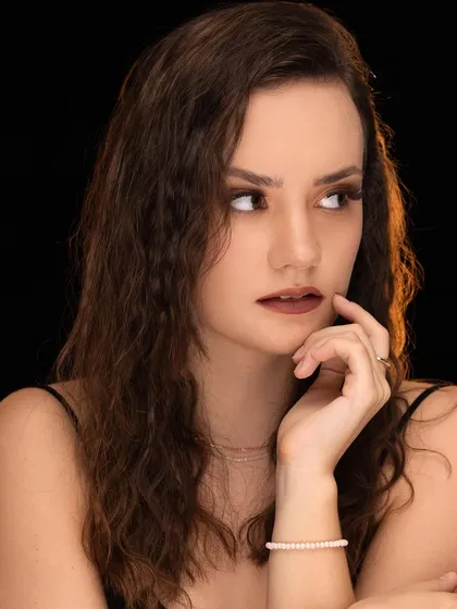 A pensive portrait of a model against a black background, with warm light highlighting her features.