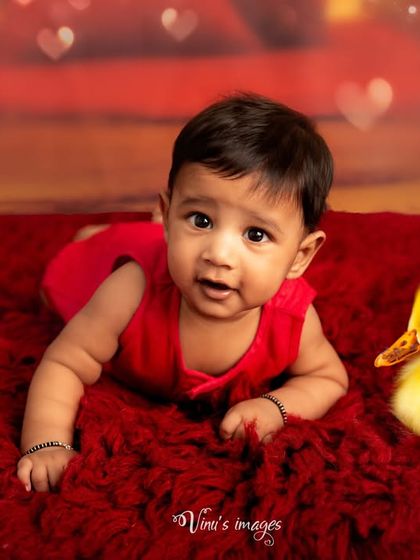 Tummy time with some feathered friends. This cute infant portrait captures a baby's curiosity as he lies on a bright red rug with two little ducklings.