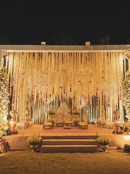 A mandap that is a haven of enchantment. The stage is framed by two large floral Christmas-tree-style installations, with a backdrop of thousands of hanging floral strings.