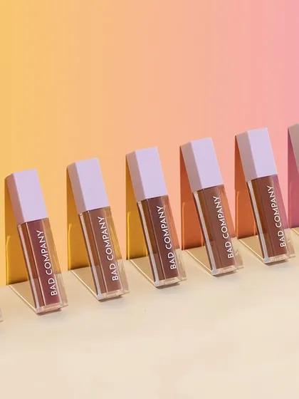 A visually pleasing shot of liquid lipsticks arranged diagonally with a colorful, multi-toned background. The hard light creates sharp shadows, adding a graphic and modern touch.