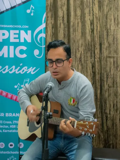 An adult student performs a song on his acoustic guitar with a microphone set up for vocals at our HSR branch open mic.