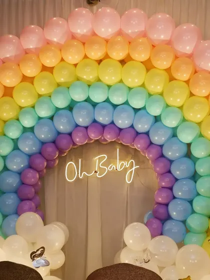 An adorable 'Oh Baby' themed setup for a baby shower. A beautiful rainbow made of pastel balloons serves as the backdrop, with a neon sign adding a modern and sweet touch.