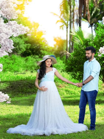 A beautiful couple's portrait in a garden, with the mother-to-be in a light blue gown and hat. The natural light creates a soft, romantic feel.