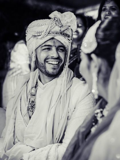 A happy black and white candid of the groom during the wedding ceremony.